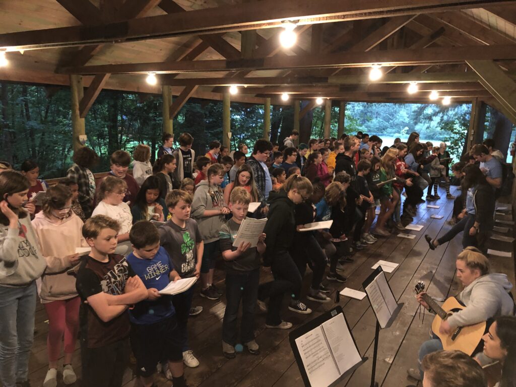 A gathering of campers and staff sing along to guitars during a chapel service
