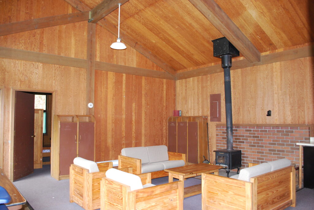 An indoor view of the Saint Clare common area. There are couches and chairs situated around a coffee table, and a small wood-burning fireplace.