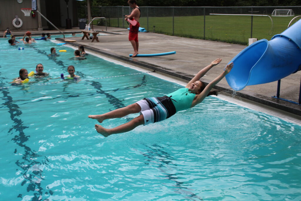 An action shot at the pool: the camper is mid-air, about to splash into the pool after sliding down the slide