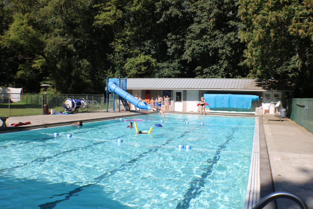 A view of the pool on a sunny day. Dividers separate the three depths, and there is a slide at the deepest end