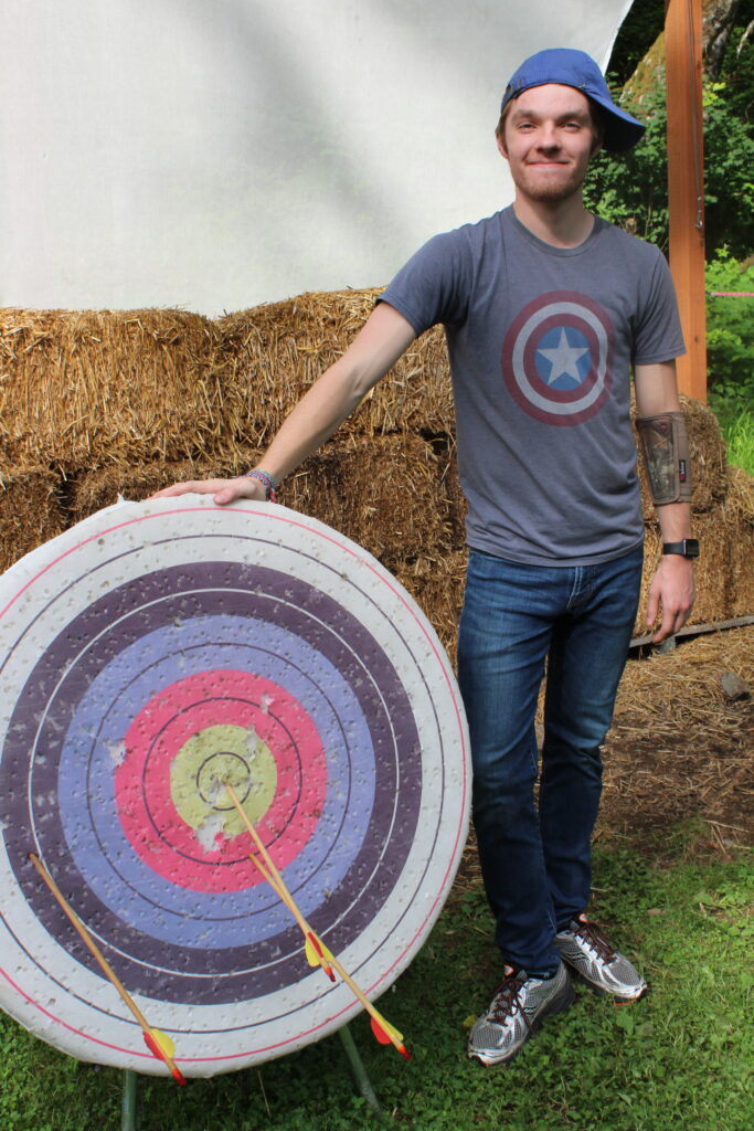 A counselor stands next to bullseye they shot with a bow and arrow